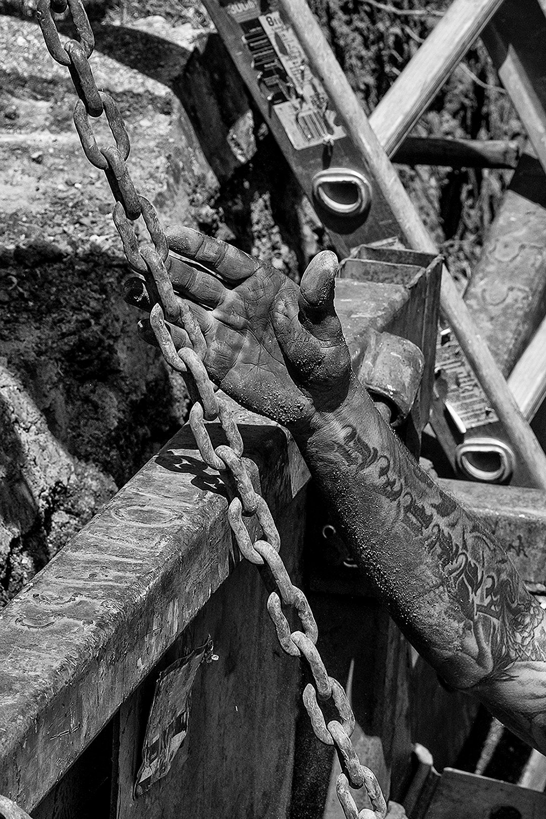 Artistic photograph of construction worker's arm reaching up from below ground while working, the arm is decorated with tattoos.