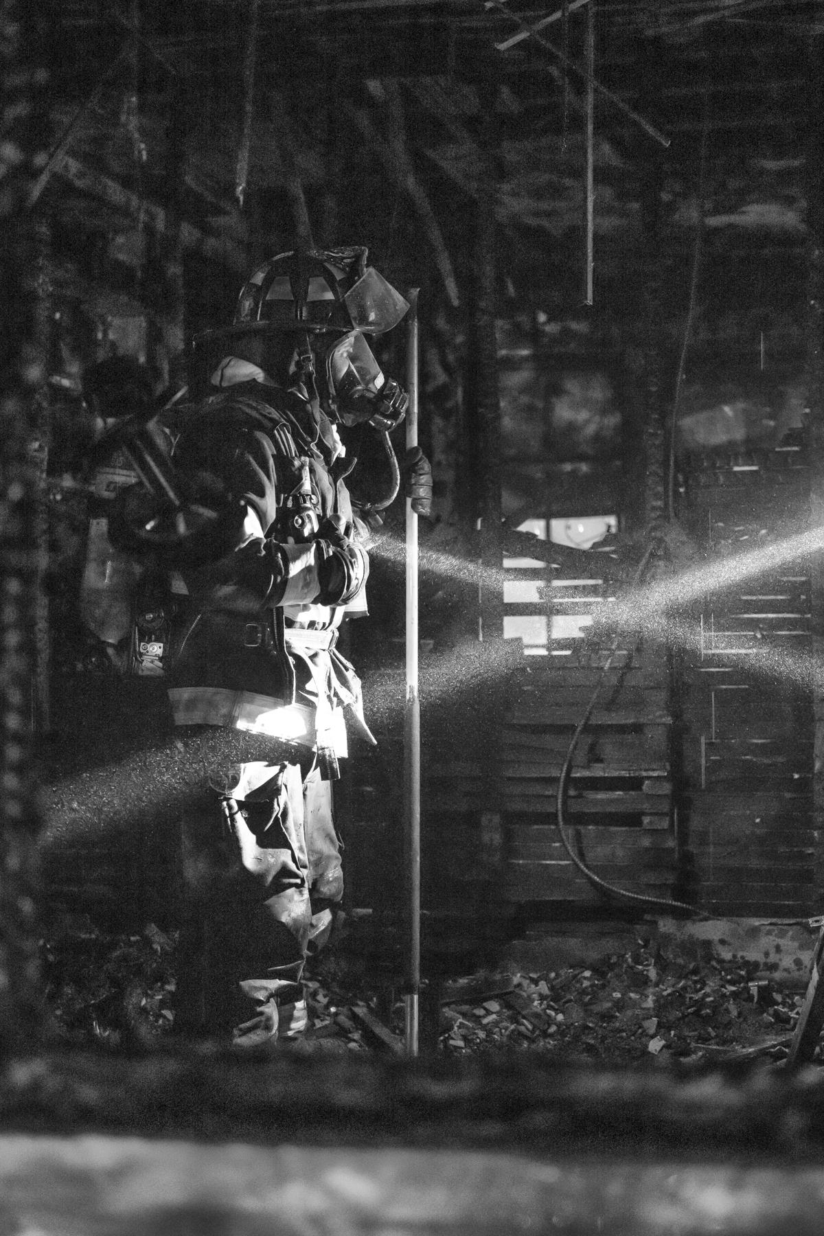 A firefighter shines a light through burnt remains of a building.